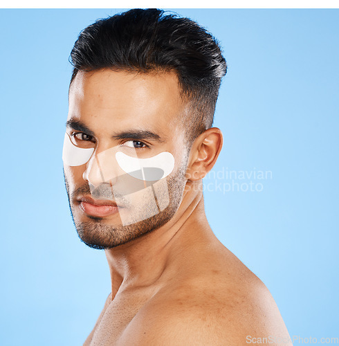 Image of Eye patches, skincare and portrait of man standing in studio doing a cosmetic beauty routine. Self care, healthy and male model doing face treatment with a facial product isolated by blue background.
