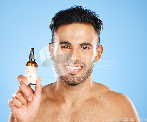 Image of Indian man, serum and skincare with smile for natural beauty, organic facial and wellness with blue studio background. Body care, male and with cosmetic oil for smooth skin, glow and happy to hydrate