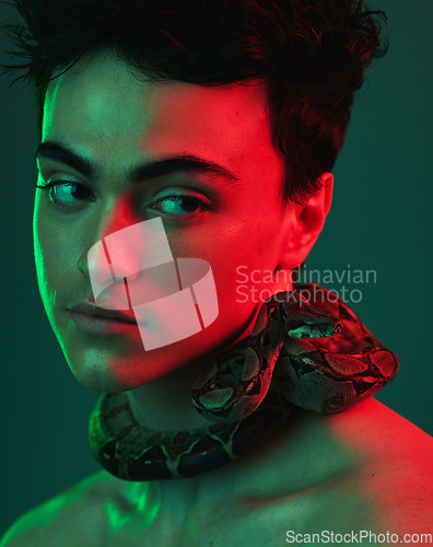 Image of Beauty, snake and model in a studio with neon light of green and red color posing with a serpent. Skincare, face and man from Mexico standing with a reptile on his neck isolated by a green background