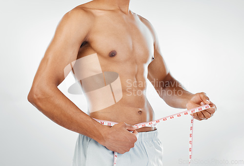 Image of Man, measuring tape with weightloss and diet, body wellness and healthy lifestyle, weight check with bare abdomen. Fitness, health and muscle, shirtless and abs with fat or slim in studio background.