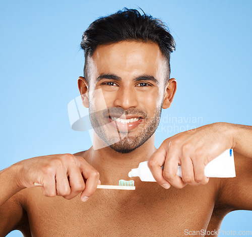 Image of Mouth, dental and man brushing teeth in studio for wellness, health and grooming on blue background. Portrait, face and teeth of indian guy happy with oral cleaning product, toothpaste and mockup