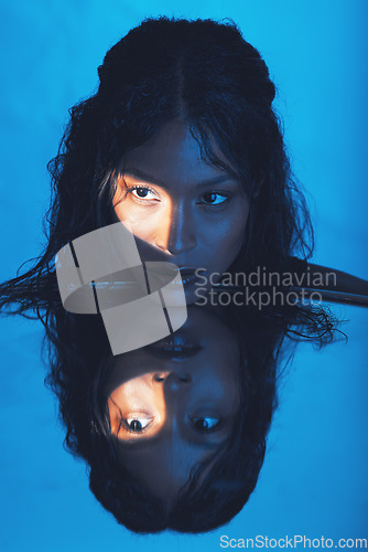 Image of Beauty, woman and light on face reflection with mirror for edgy cosmetics, skincare or advertising. Shadow, thinking and spotlight on beautiful cosmetic black model with blue studio background.