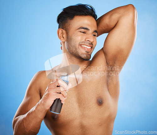 Image of Smile, happy and man spray deodorant for hygiene, fresh scent or body care after shower on blue studio background. Perfume, product and male model from India spraying armpit to prevent smell or odor