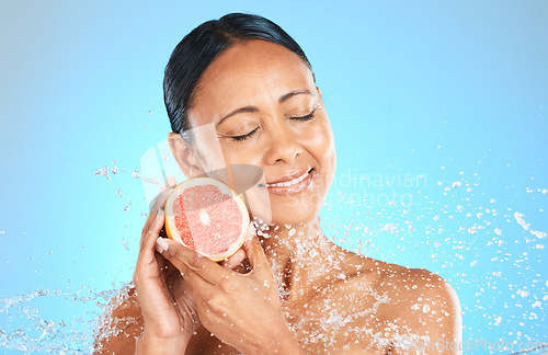 Image of Skincare, beauty and woman with grapefruit in studio for cleaning, grooming and wellness against blue background. Face, water and fruit product with girl skin model relax, smile and facial, treatment