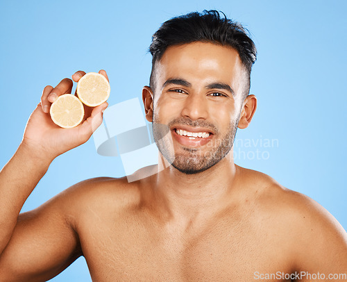 Image of Face, skincare and orange with a man model in studio on a blue background to promote natural beauty. Portrait, fruit and wellness with a handsome young male posing for a health product or treatment