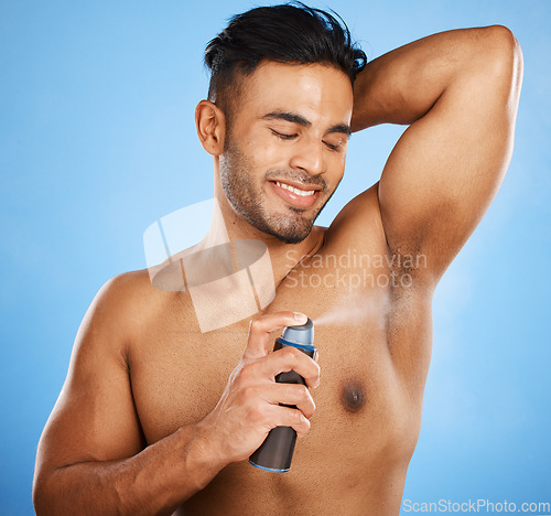 Image of Deodorant, beauty and grooming with a man model using antiperspirant in studio on a blue background. Body spray, aerosol and smell with a handsome young male spraying a scent product to his underarm