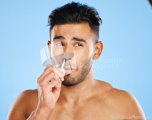 Image of Beauty, hair and nose tweezers with man in a studio for cleaning, wellness and skincare against a blue background. Face, hair removal and mexican model grooming, hygiene and tweezer pamper treatment