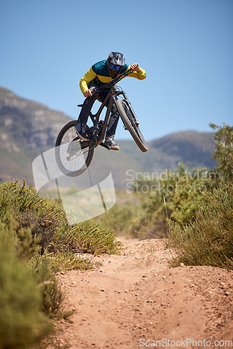 Image of Bike, bmx and fitness with a man biker on a dirt trail or track taking a jump with a mountain bike. Sky, nature and cycling with a mountain biker jumping in midair while riding outdoor for adrenaline