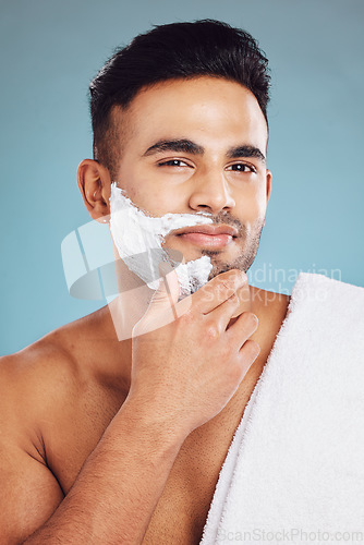 Image of Face, beauty and shave with a man model in studio on a blue background for shaving or grooming. Portrait, skincare and hair removal with a handsome young male shaving his beard in the bathroom