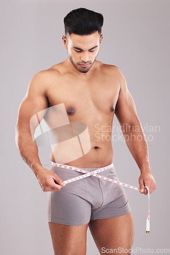 Image of Weightloss, fitness and man with measure tape standing in a studio with a gray background. Health, strong and athlete with a healthy, exercise and diet lifestyle measuring his weight after a workout.