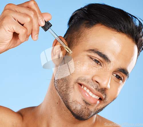 Image of Oil, skincare and man with serum for face against a blue studio background. Wellness, happy and young model with a liquid with hyaluronic acid for growth of beard, cleaning and dermatology health