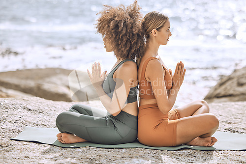 Image of Yoga, meditate and fitness women at the beach, ocean and sea feeling mindfulness and peace. Diversity of relax and peaceful girl friends in nature by the water meditating for spiritual wellness