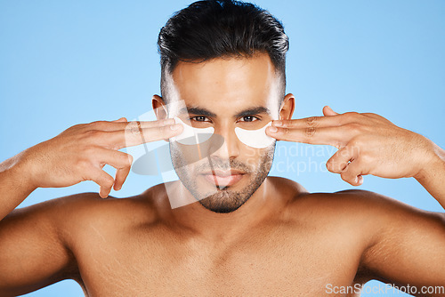 Image of Man, eye patches and beauty for skincare, cosmetics or facial products against a blue studio background. Portrait of isolated male model in care for eyes applying patch for healthy skin or treatment