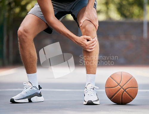 Image of Pain, basketball and man with knee injury standing on outdoor court, holding leg. Sports, fitness and athlete with joint pain, injured and hurt in training, workout and game on basketball court