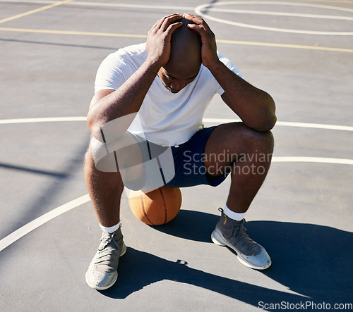 Image of Basketball, sports and depressed man on court with hands on head after loss, fail and bad game. Fitness, sadness and upset black man sitting on ball on outdoor basketball court, frustrated and mad