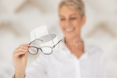 Image of Vision, blur and woman holding glasses in an optometry store buying prescription lenses. Retail, optometrist and senior lady trying spectacles in optician, optical or eyewear shop for eye care.