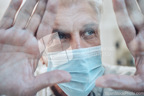 Image of Hands, covid and quarantine with a senior man in a mask standing behind glass in a house during lockdown. Window, sad and isolated with a mature male in a retirement home during corona virus pandemic
