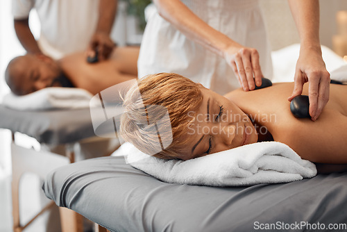 Image of Spa, couple and massage for health and wellness while on bed for hot stone or rock therapy on back for zen, peace and relax. Man and woman customer in beauty salon for physical therapy and self care