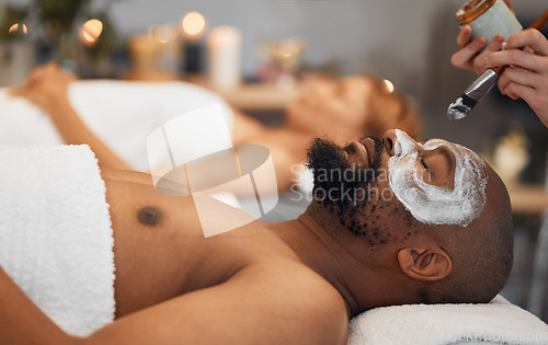 Image of Skincare, wellness and black man getting a facial at a spa for relaxation, calm and satisfaction. Beauty, luxury treatment and couple massage at beauty salon together, skincare products on mans face