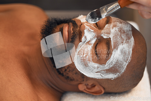 Image of Facial, skincare and relax with black man in spa for beauty, luxury and mud mask. Wellness, therapy and health with male and beautician brush cosmetics product on face for peace, massage and salon