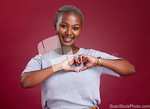 Image of Hands, heart and love with a model black woman in studio on a red background to promote health or wellness. Portrait, smile and hand sign with a young female posing to endorse romance or cardio