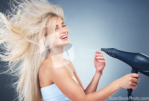 Image of Beauty, hair care and woman on blue background with hair dryer, smile and healthy blonde salon hair style. Health, wellness and luxury care for happy model hair, color treatment, shampoo and dry hair