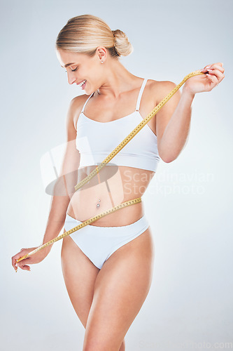 Image of Measuring tape, weight loss and woman measuring waist, stomach and belly for fat or ab muscle growth. Fitness model, healthy girl body and happy result of exercise training on gray studio background