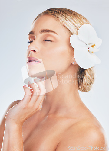 Image of Skincare, wellness and face of a woman with an orchid for health, beauty and dermatology against a grey studio background. Spa, flower and girl model with a natural plant for care for skin and body