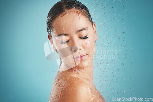 Image of Face, shower and cleaning with a woman in studio on a blue background for hygiene cleansing or hydrating. Water, bathroom and wellness with an attractive young female washing in a bathroom for care