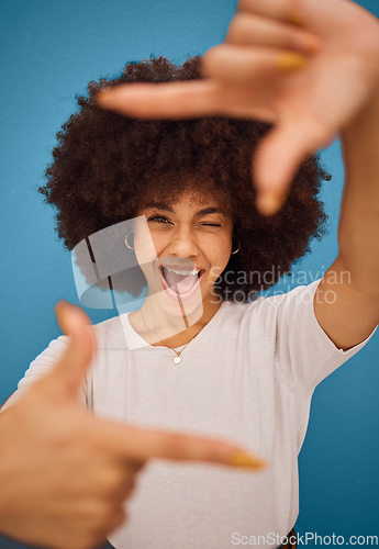 Image of Black woman, hand frame afro and studio beauty with wink, smile and comic pose by blue background. African model woman, sign hands and funny portrait with happy face, photography and play by backdrop