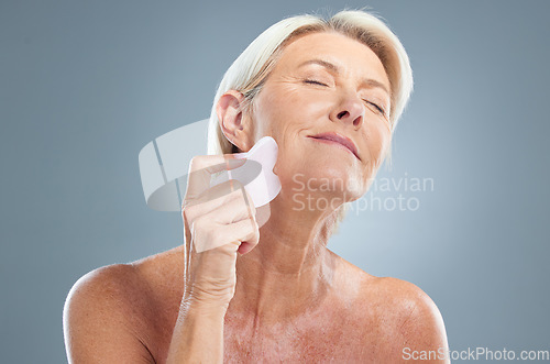 Image of Face, beauty and massage with a senior woman in studio on a gray background for skincare to relax. Skin, wellness and antiaging with a mature female using a massaging tool for natural treatment