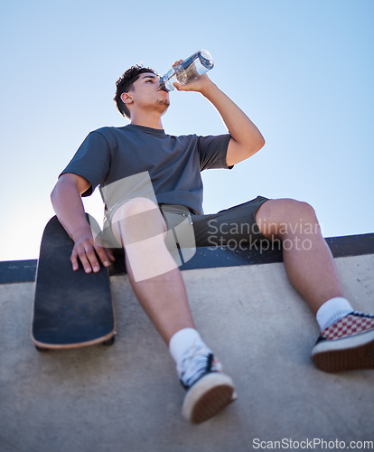 Image of Skateboard, young man and drinking water bottle, relax and on break on sunny day outdoor. Male, skater and athlete hydrate, thirsty and sports for wellness, health and have fun in summer.