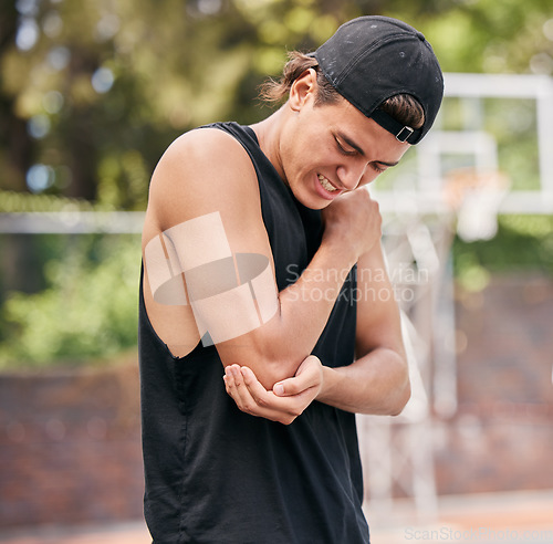 Image of Sport injury, basketball and man in pain while playing on basketball court, fitness and hurt elbow outdoor. Young athlete holding arm, sore and exercise accident, sports and training in park.