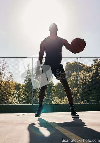 Image of Basketball, sports and man in a park for training, cardio and exercise with a ball during summer. Dark silhouette of a professional athlete with freedom and energy for a sport on a basketball court