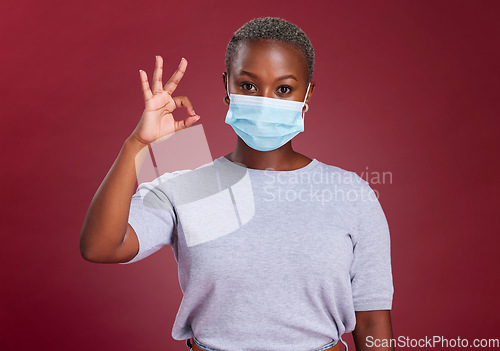 Image of Black woman, covid and ok sign with face mask for approval, yes and safety with hand gesture for health and wellness. Portrait of African model for covid 19, corona and virus compliance in studio