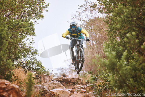 Image of Mountain bike, sports and fitness with a man adrenaline junkie riding in the woods or forest in nature. Sky, training and exercise with a male athlete on a bike for trail riding or adventure