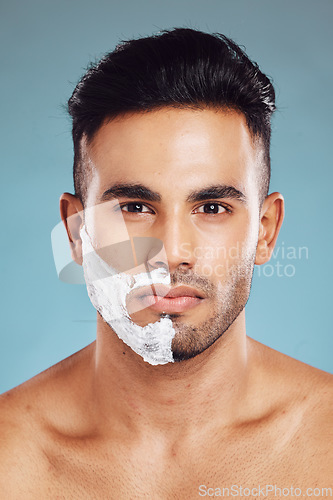 Image of Portrait, skincare and man shaving in studio on blue background for facial hair grooming in India. Healthy, products and young face model shaves beard and mustache in self care routine with cream