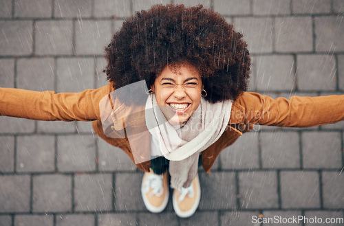 Image of Black woman, stand to feel rain and happy in city in winter with smile, afro or trendy fashion. Woman, outdoor above or happiness in drizzle, splash and face in metro, urban or town with natural hair