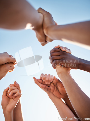 Image of Low angle, group and holding hands in support, trust huddle and motivation for global success, volunteer community or diversity. People, friends or teamwork collaboration in circle for climate change