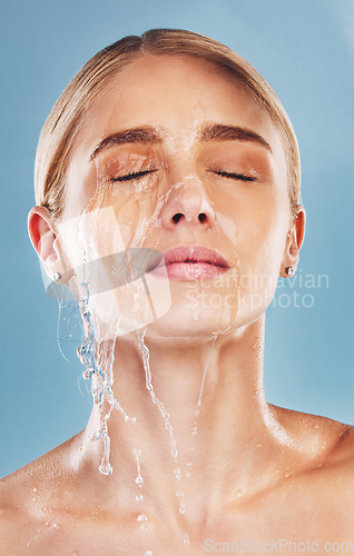 Image of Water, skincare and face of a woman with a splash for cleaning, treatment and care against a blue studio background. Wellness, health and girl model with luxury facial dermatology to relax for beauty