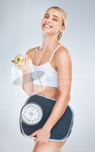 Image of Health, lose weight and woman with an apple and scale for body goal, motivation and nutrition against a grey studio background. Food, happy and portrait of athlete model with smile for fruit and diet