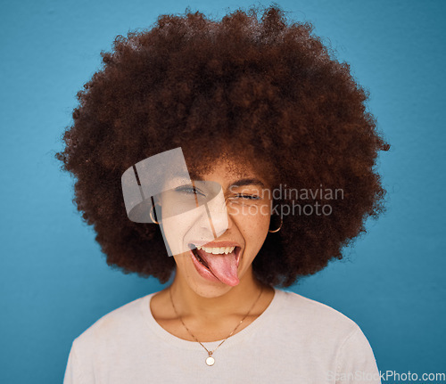 Image of Face, portrait and woman with tongue out being silly and goofy on a blue studio background. Amusing, comic and crazy african american female making a funny, humour face on a backdrop