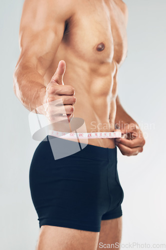 Image of Fitness, thumbs up and man measuring body after training, workout and exercise. Healthy, wellness and strong muscular male with measuring tape on waist for diet, weight loss and body care in studio