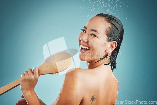 Image of Woman, singing and shower in studio for wellness, skin and body care on a blue background, happy and relax. Singer, bathroom and water splash karaoke by portrait of asian girl having fun and grooming