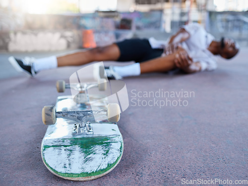 Image of Skateboard, skater and knee injury in street, city or outdoors after failed stunt or accident. Skateboarding, sports and black man with sore leg, joint inflammation or muscle pain at urban skate park