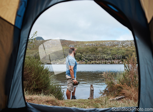 Image of Man by lake from tent view, outdoor and camping for adventure, vacation or holiday in nature. Explorer, binocular and morning for sightseeing by river, dam or water on natural rest, relax or retreat