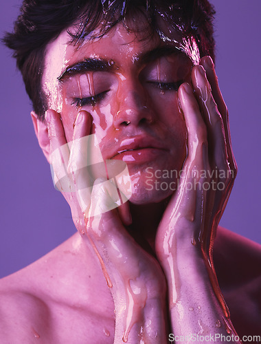 Image of Model, man and skincare with honey dripping on face, cosmetics and organic beauty by purple backdrop. Skin, cosmetic and facial with natural moisturizer for exfoliate for health, wellness and glow