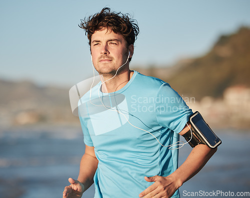 Image of Running, music and man athlete at beach with headphones run by the ocean with audio streaming. Mobile radio, web podcast or training song of a runner athlete listening to a track on an outdoor run