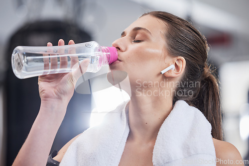 Image of Gym, fitness and woman with earphones drinking water from bottle, cardio workout while listening to music on streaming radio. Sports, exercise and drink of water for healthy lifestyle while training.