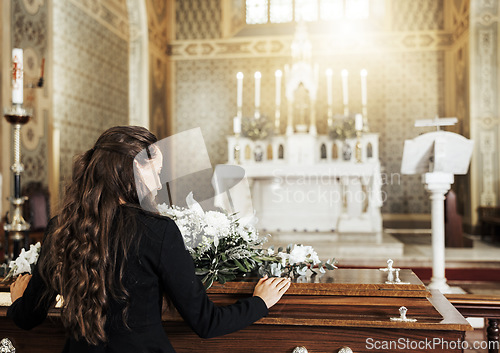 Image of Funeral coffin, death and woman in church after the loss of family, friend or loved one from cancer. RIp, mourning and back view of female with flowers on wood casket in cathedral for burial ceremony